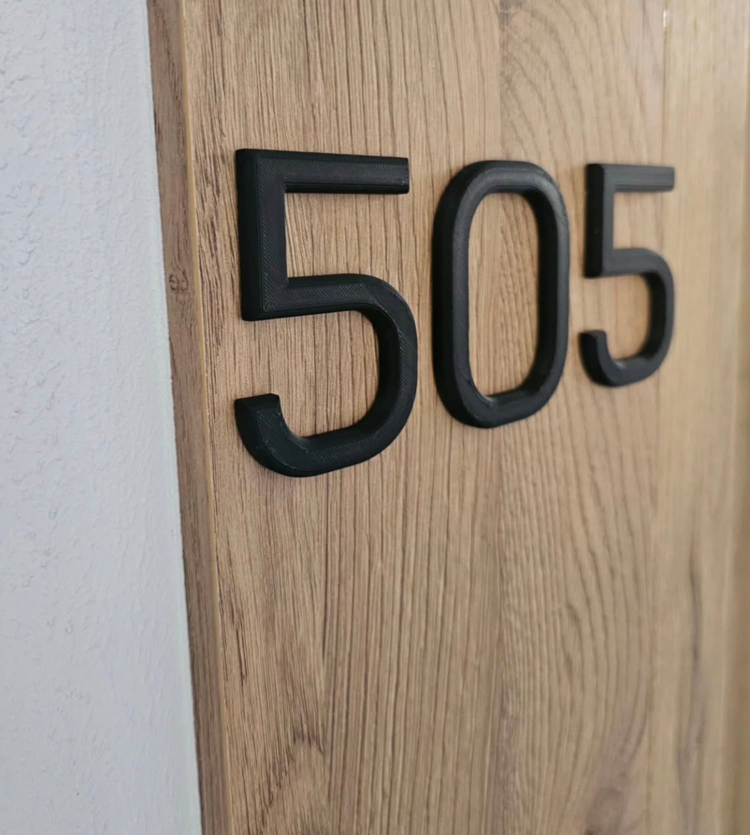 3D printed door number 505 mounted on an oak apartment door
