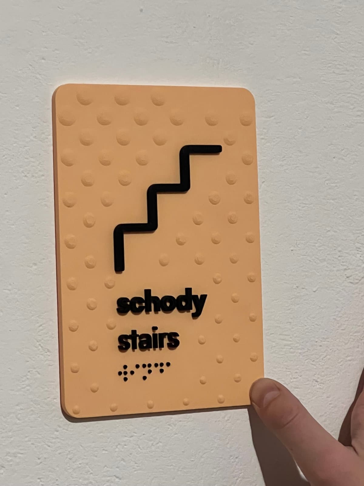Tactile stairs wayfinding sign with a pictogram and Braille, held in hand.