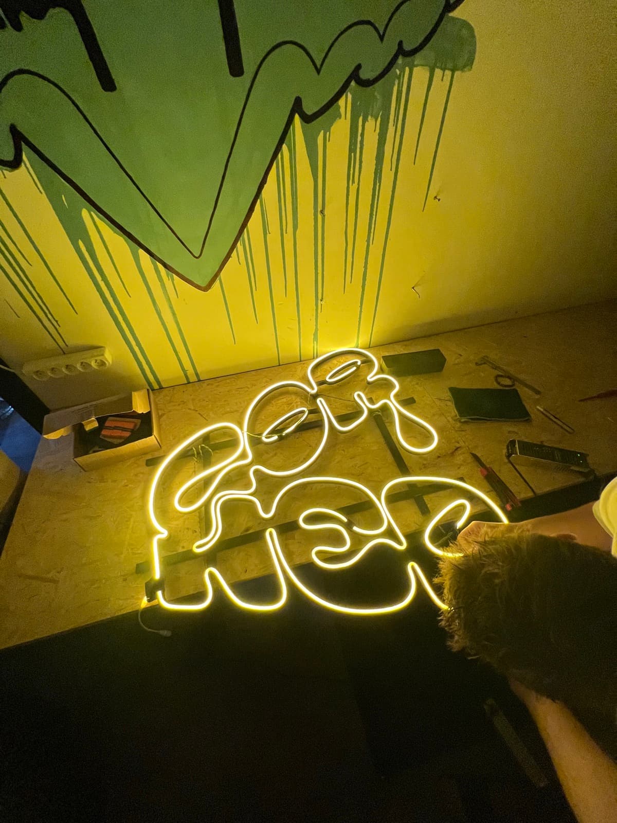 The finished CORNER LED sign glowing yellow in the tattoo studio, against the wall graffiti.