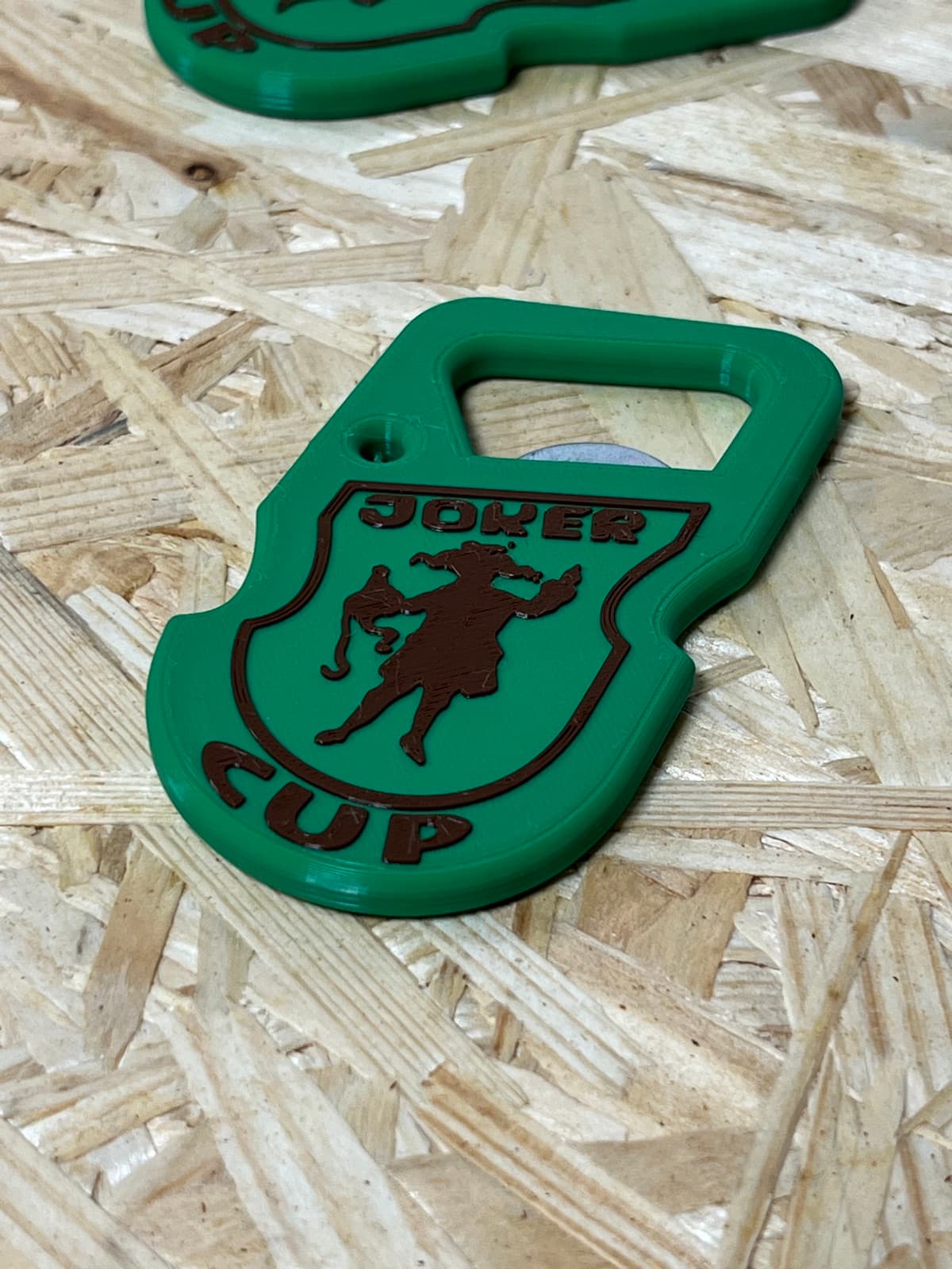 Close-up of a printed JOKER CUP bottle opener showing the embossed crest and lettering on the green body.