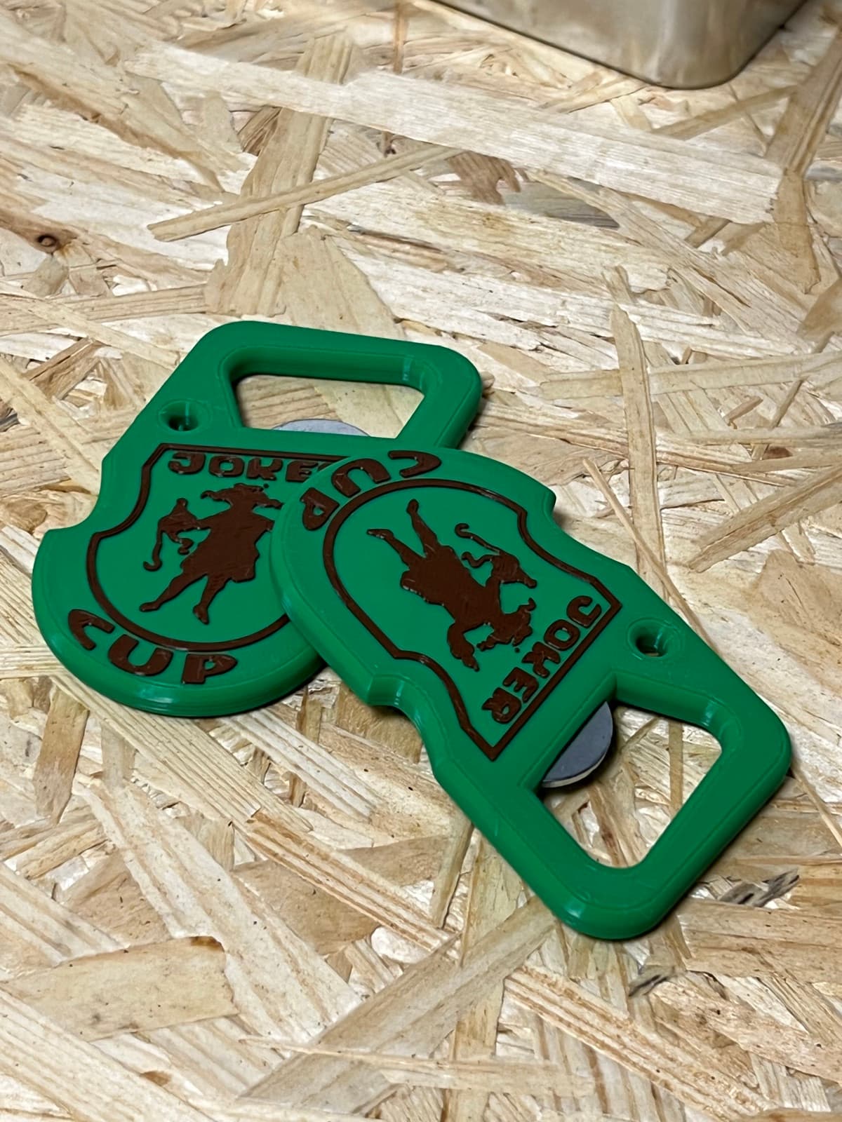 Two green openers, the front with the crest and the back showing the embedded magnet and metal lever.