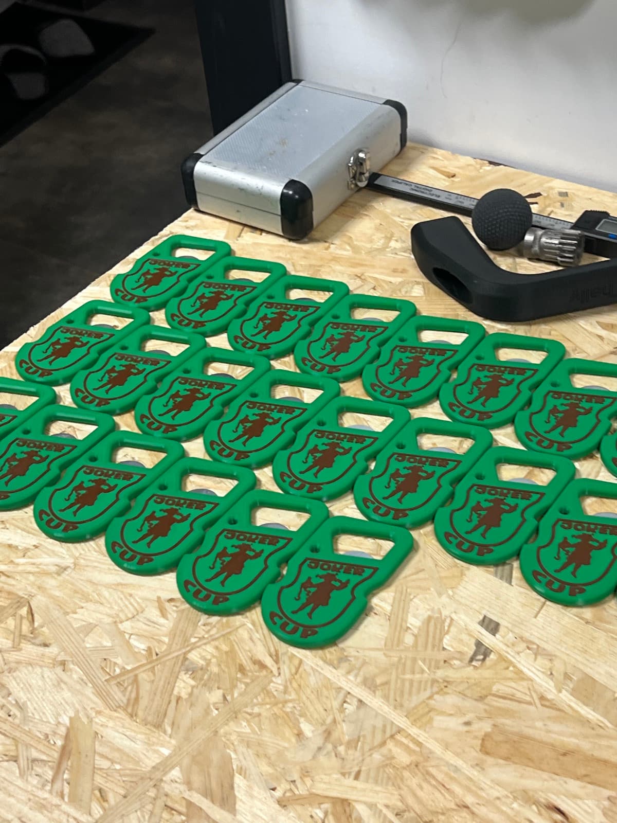 A batch of several dozen green openers laid out on the workbench next to tools.
