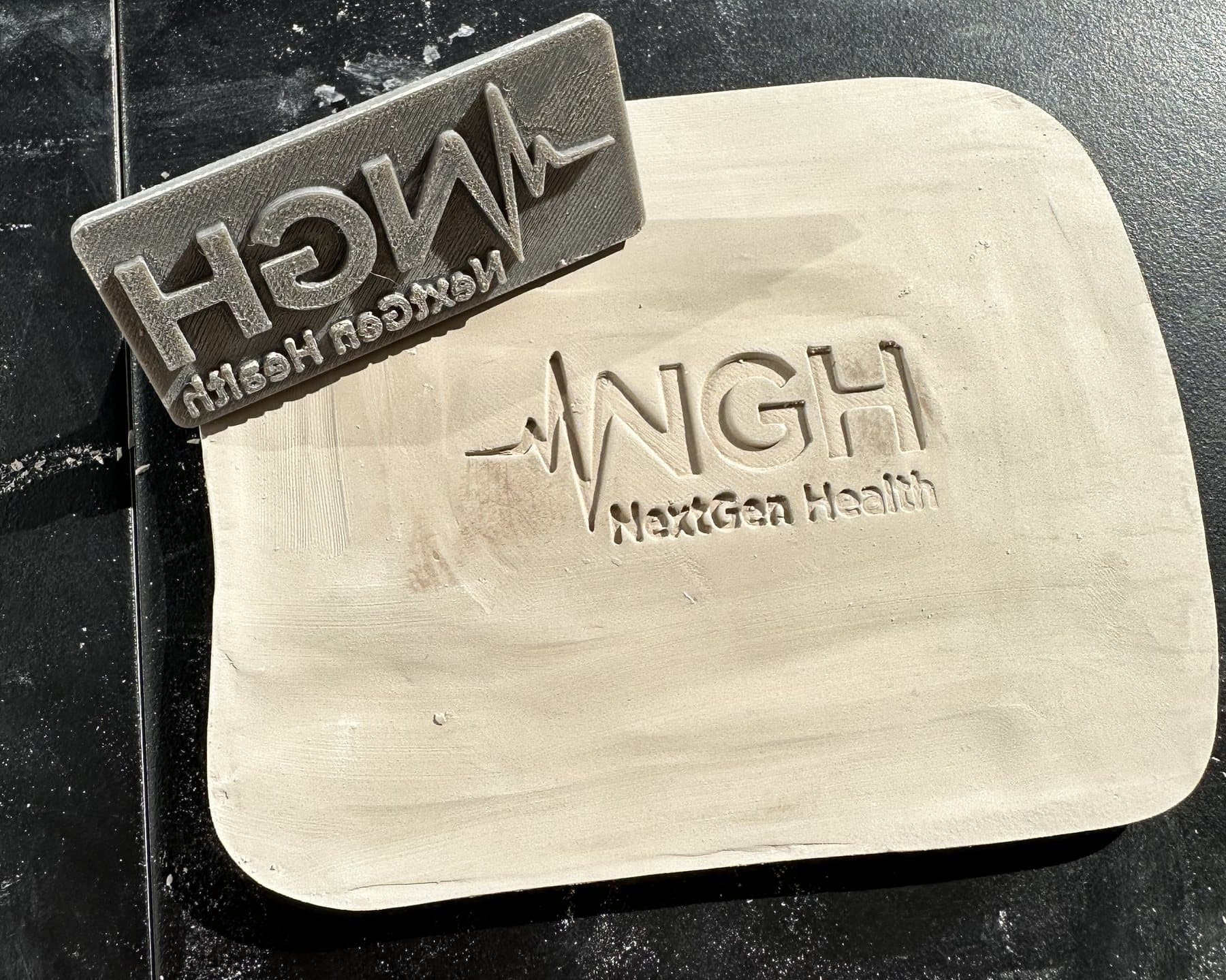 The stamp next to a fresh impression in a slab of clay for a ceramic business card.
